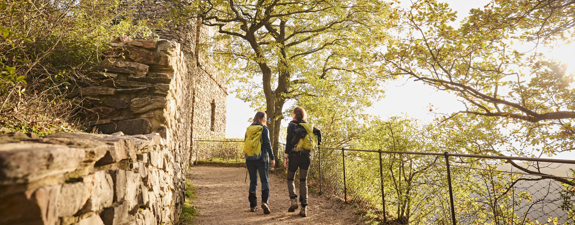 In herbstlicher Atmosphäre laufen zwei Wanderinnen auf dem Rheinsteig zur Burgruine Rossel