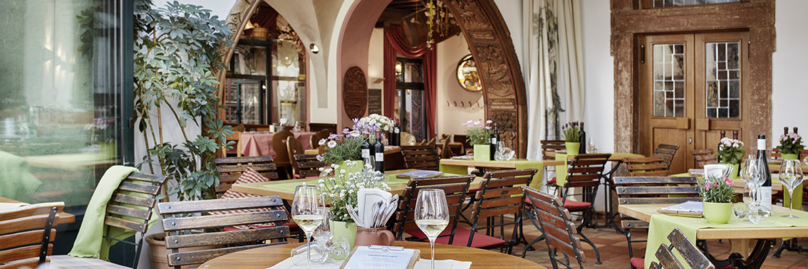 Breuer's Rüdesheimer Schloss Blick von der Terrasse ins Restaurant vom Breuer's Rüdesheimer Schloss. Das Ambiente sieht sehr gemütlich und einladend aus. Auf den Tischen stehen frische Blumen