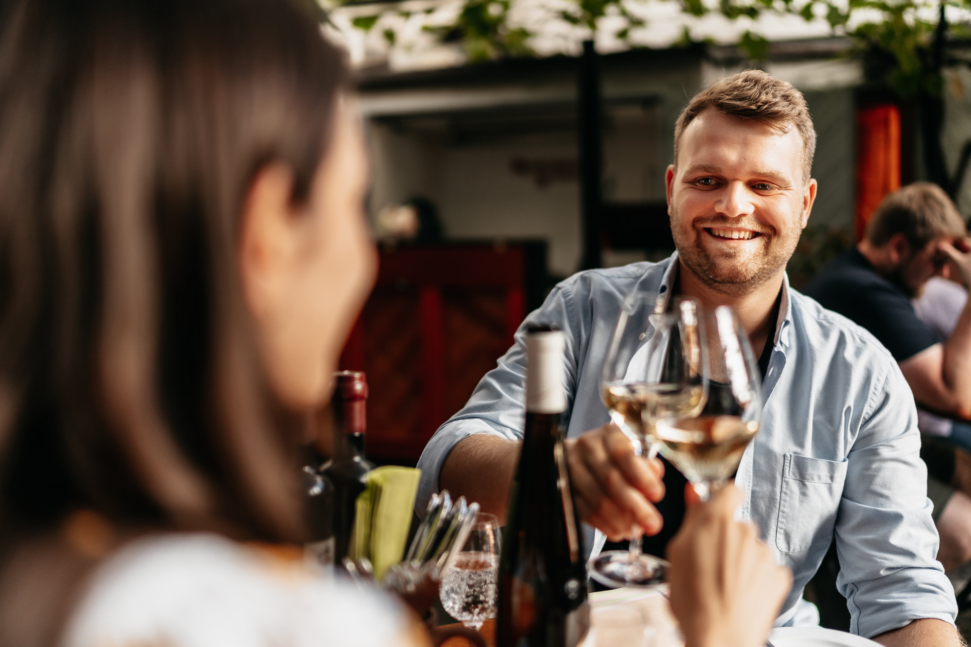 Eine Frau und ein Mann sitzen in einem Innenhof beim Winzer und prosten sich zu. Der Hintergrund ist verschwommen.