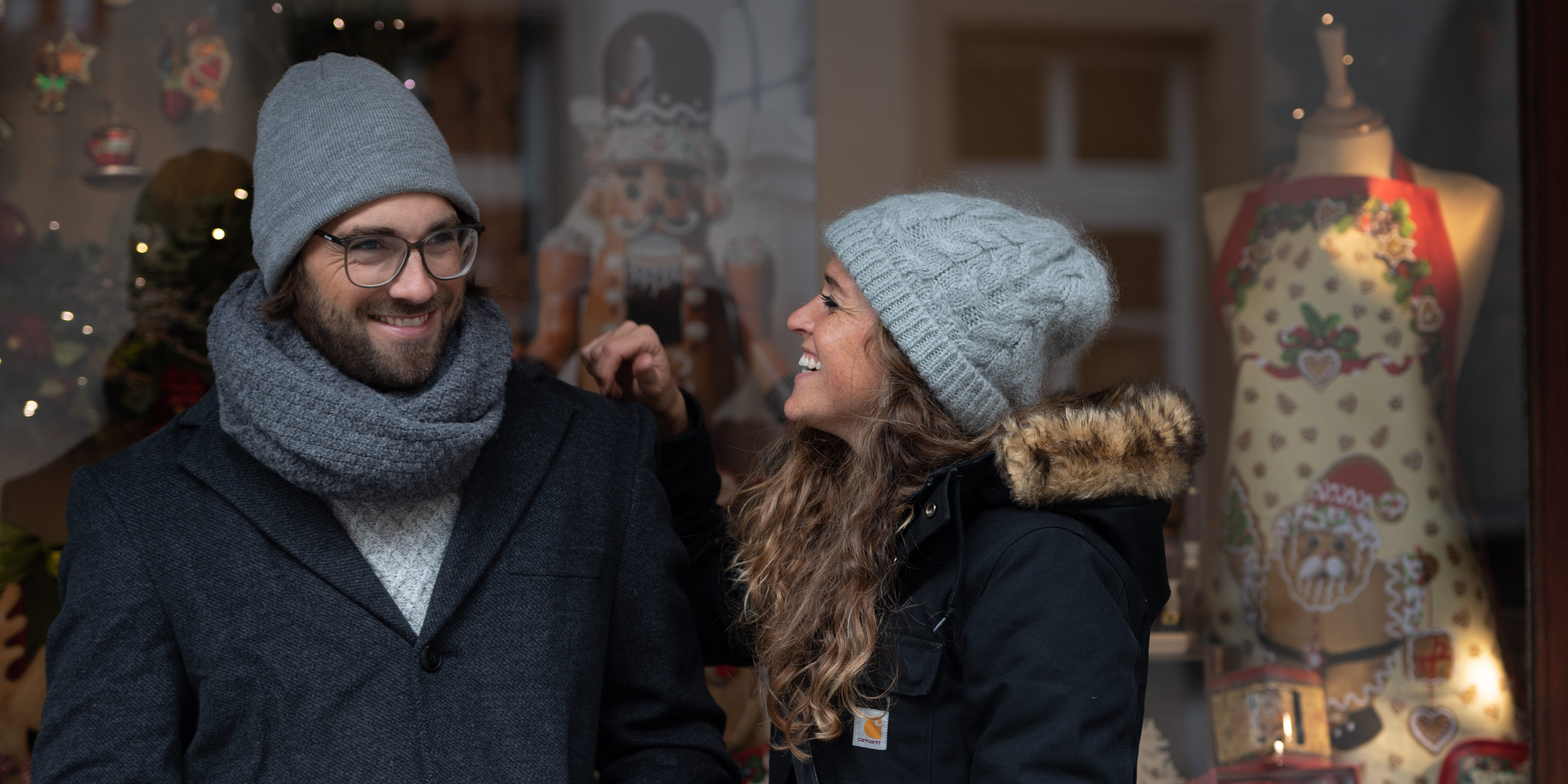 Ein Paar steht mit Glühwein in der Hand vor einem weihnachtlich geschmückten Schaufenster