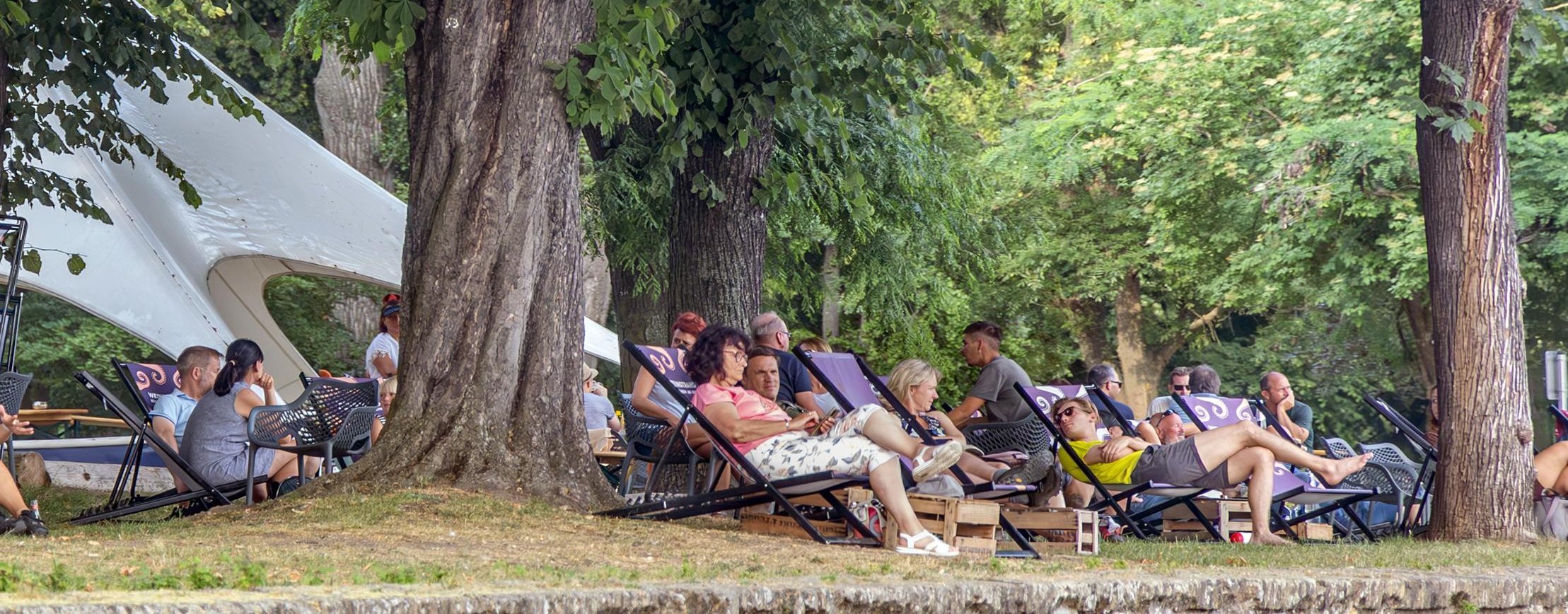 Weinstrand am Hafenpark Der Hafenpark in Rüdesheim an einem schönen Sommertag. Viele Gäste sitzen auf Liegestühlen und genießen Ihre Getränke.