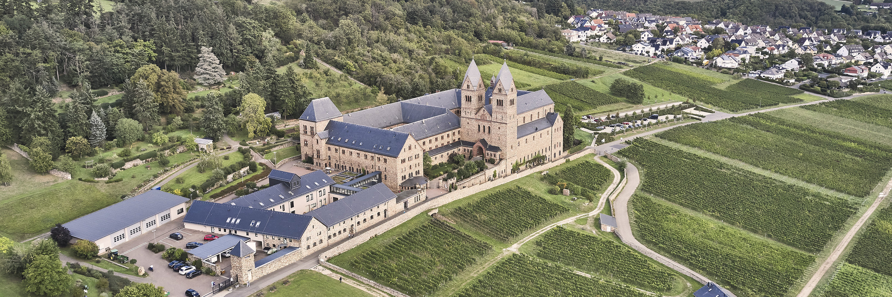 Abtei St. Hildegard Die Luftaufnahme der Abtei St. Hildegard zeigt das Kloster von oben umgeben von Weinbergen bei leicht bewölktem Himmel