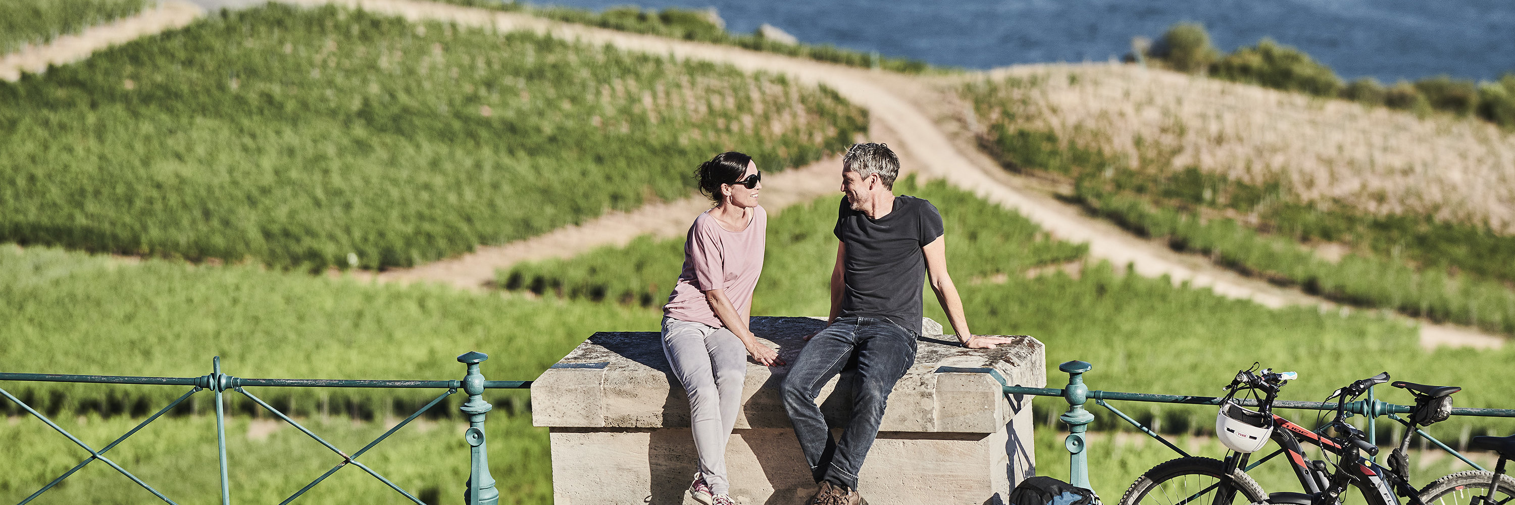 Radtour zum Niederwalddenkmal Ein Paar macht während einer Radtour eine Pause beim Niderwalddenkmal. Sie sitzen gemütlich auf einem Stein und haben die Aussicht auf den Rhein und die Weinberge.