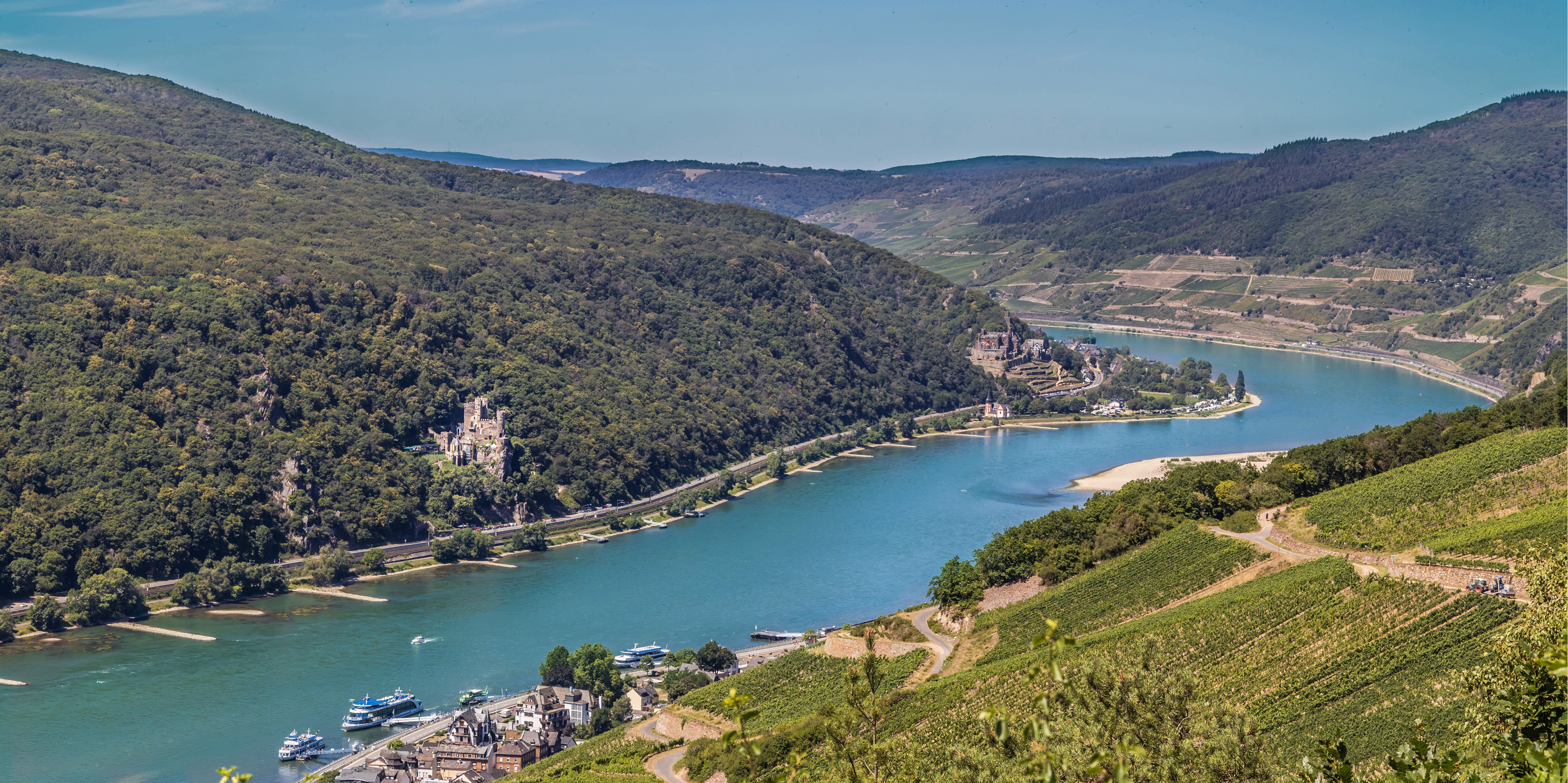 Blick auf den Rheinverlauf bei sonnigen Wetter. Zu sehen ist Assmannshausen und auf der anderen Rheinseite die Burg Rheinstein