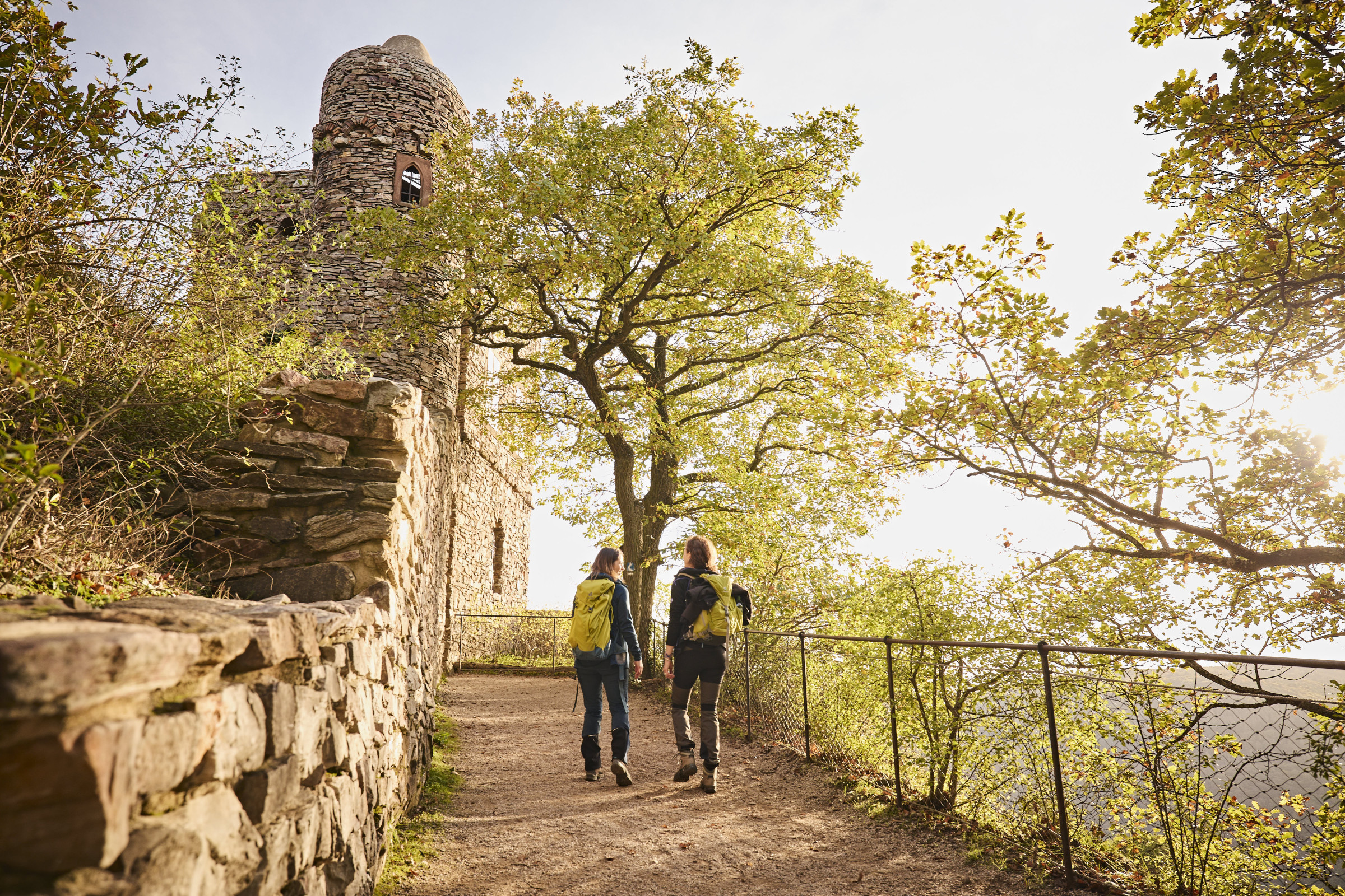 In herbstlicher Atmosphäre laufen zwei Wanderinnen auf dem Rheinsteig zur Burgruine Rossel